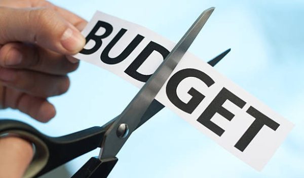 Scissors cutting the word "budget" on blue background. You may also like: